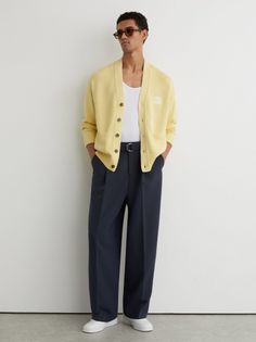 Man in a yellow cardigan, white tank top, and dark pants with sunglasses