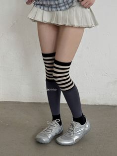 Person wearing a pleated skirt, plaid shirt, and striped knee-high socks indoors