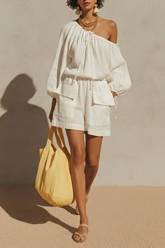 Woman in a white off-shoulder top and shorts with a yellow tote bag