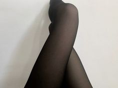 Person wearing black tights with legs crossed against a white background