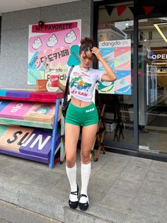 Woman in a crop top and green shorts standing outside a colorful shop