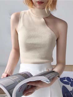 Woman with short blonde hair wearing a cut-out sleeveless top and white skirt, holding a magazine