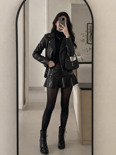 Woman in a black leather jacket and mini skirt taking a mirror selfie