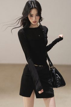 Woman in a black top and skirt with a black handbag, hair blowing in the wind