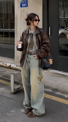 Woman in a brown leather jacket and baggy jeans holding an iced coffee on a street
