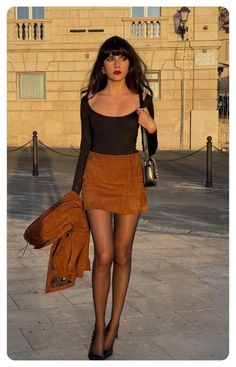 Woman with long dark hair in a suede skirt and black top on a city street