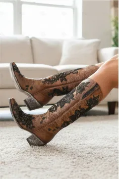 Close up of legs wearing brown cowboy boots with black lace pattern