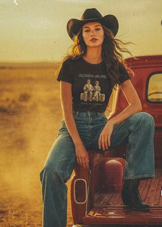Woman in a cowboy hat and jeans sitting on the tailgate of a red truck