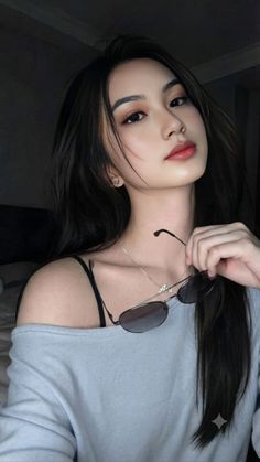 Woman with long dark hair wearing an off-shoulder top and holding sunglasses
