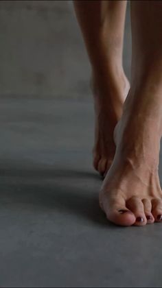 Close up of bare feet with dark nail polish walking on a dark floor