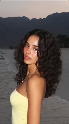 Woman with curly hair on a beach with mountains in the background