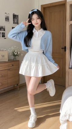 Woman in a blue cardigan and white skirt posing indoors