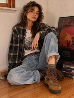 Woman in a plaid shirt and loose jeans sitting on a wooden floor