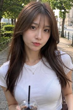 Woman with long brown hair in a white t-shirt holding a drink outdoors