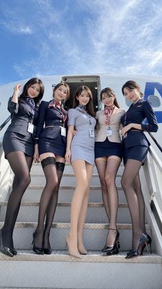 Five women in flight attendant uniforms posing on airplane stairs