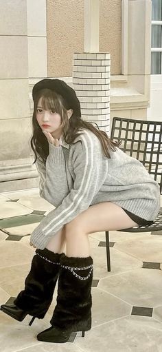 Woman in a black beret and gray sweater with furry leg warmers sitting outdoors