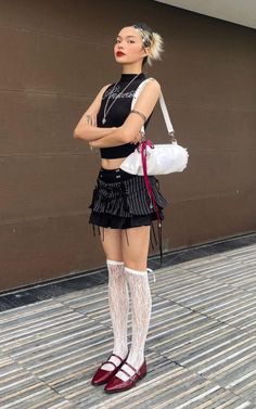 Woman in a black crop top and striped mini skirt with lace socks and red shoes