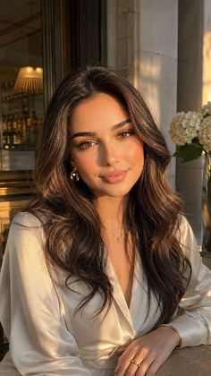 Woman with long brown hair in a white blouse, bathed in golden hour light