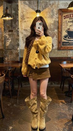 Woman in a yellow cardigan and mini skirt taking a mirror selfie in a cafe