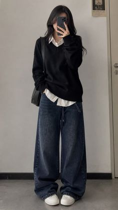 Person in a black sweater and wide leg jeans taking a mirror selfie