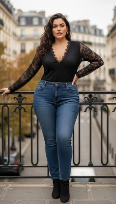 Woman in a black lace top and blue jeans posing on a city balcony