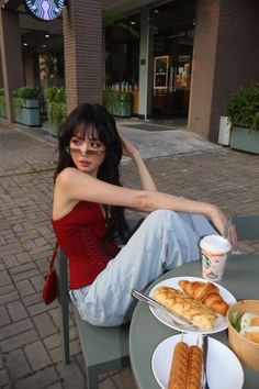 Woman with long dark hair and sunglasses sitting at an outdoor cafe table