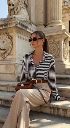 Woman in a striped shirt and beige pants sitting on stone steps next to a lion statue
