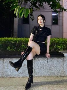Woman in a black outfit and knee high boots sitting outdoors at night