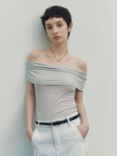 Woman with short hair wearing an off-shoulder top and white jeans