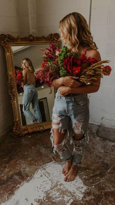 Woman in ripped jeans holding flowers, reflected in a mirror