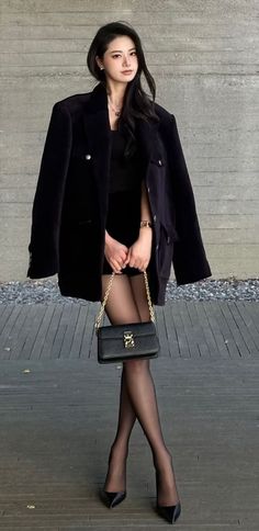 Woman in a black blazer and dress with a shoulder bag standing outdoors