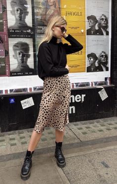 Woman in a leopard print skirt and black turtleneck standing on a street
