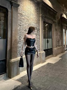 Woman in a black leather top and mini skirt walking on a street at night