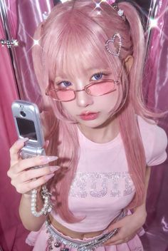 Woman with pink hair and glasses holding a flip phone, wearing a pink cropped top and mini skirt