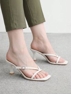 Person wearing white strappy high heels and green cropped pants indoors