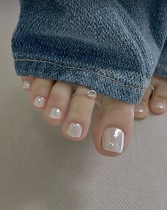 Close up of feet with white nail polish and a toe ring, wearing denim jeans