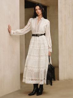 Woman in a white lace dress with a black belt and fringe bag indoors