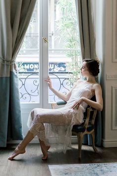 Woman in a white lace dress sitting by a window, looking outside