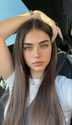 Woman with long brown hair and green eyes wearing a white t-shirt