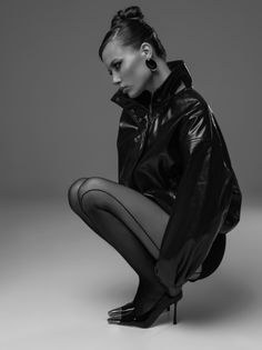 Woman in a leather jacket and tights squatting in a studio