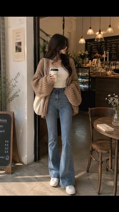Woman in a knitted cardigan and flare jeans holding a coffee cup in a cafe