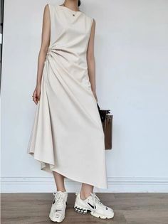 Woman in a white ruched midi dress and sneakers holding a brown handbag