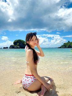 Woman in a bikini sitting on a sandy beach with clear water and blue sky