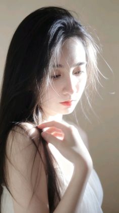 Woman with long black hair in soft backlight, touching her hair