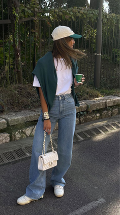 Woman in a baseball cap and wide leg jeans holding a coffee cup and handbag outdoors