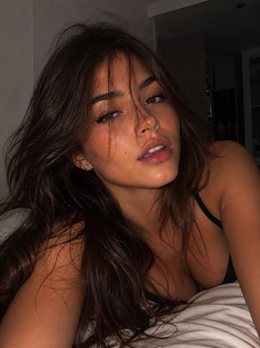 Woman with long dark hair and freckles, wearing a black bra, lying down
