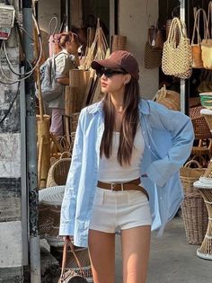 Woman in a blue shirt and white shorts wearing a baseball cap and sunglasses at a street market