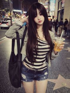 Woman with long dark hair in a striped top and distressed shorts on a city street at night