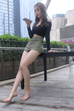 Woman in a black crop top and olive mini skirt holding a phone outdoors