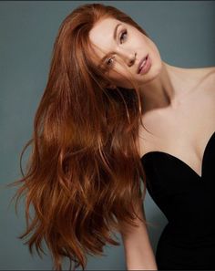 Woman with long red hair wearing a black strapless dress in a studio shot